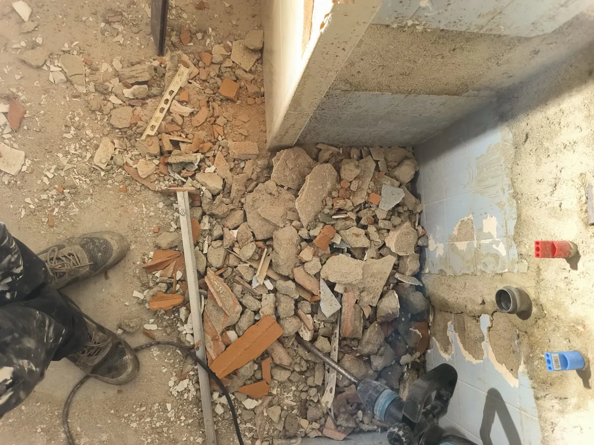 Demolição de casa de banho com entulho e tubagens à vista