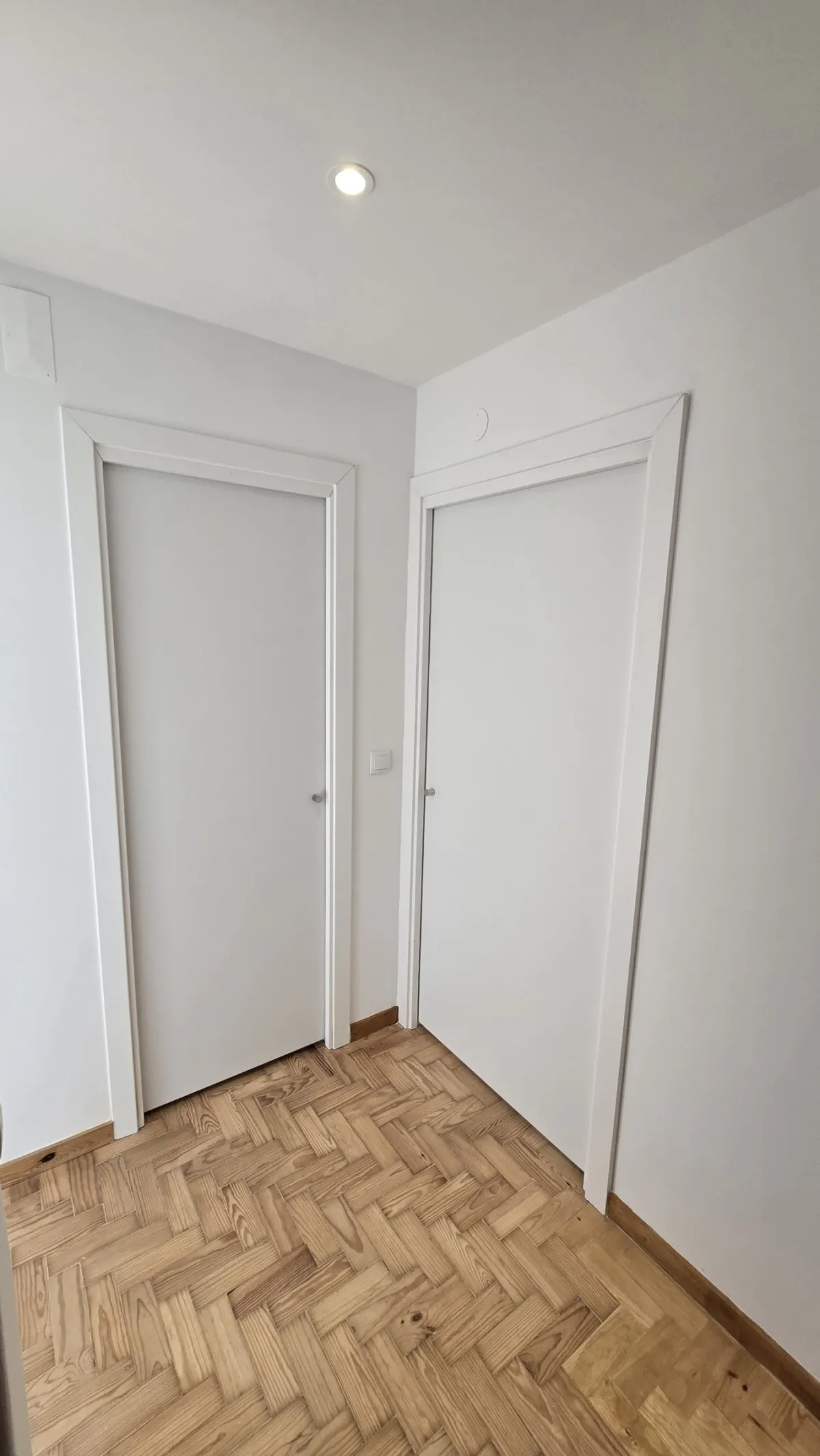 Hall de entrada com duas portas interiores lacadas a branco e parquet em espinha