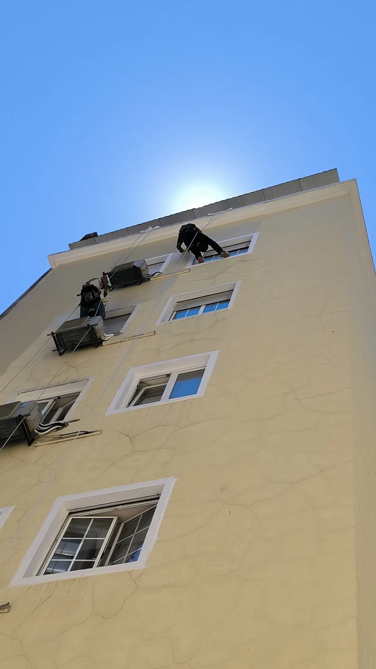 Técnicos suspensos por corda a trabalhar na fachada de um prédio