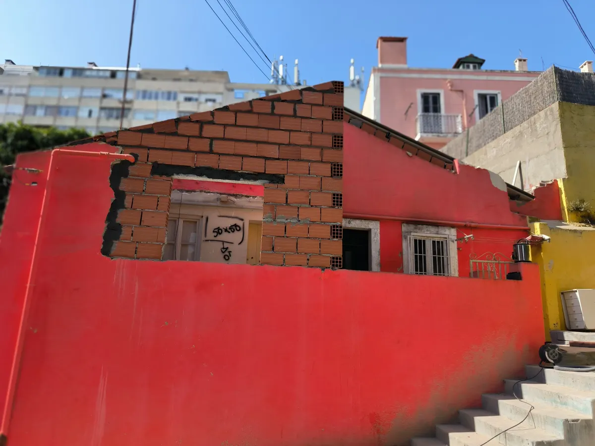 Fachada vermelha da moradia no início da obra, com a nova parede em alvenaria