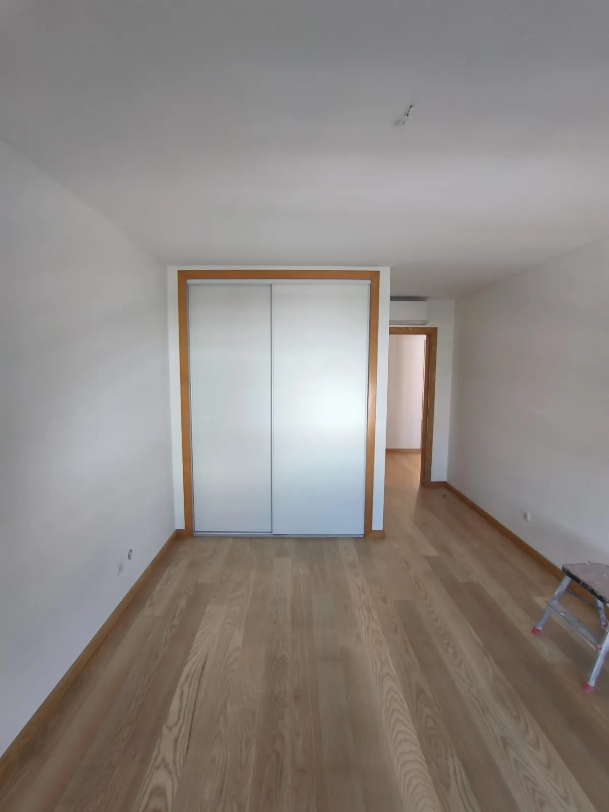 Quarto com pavimento em madeira, paredes brancas e roupeiro de portas de correr