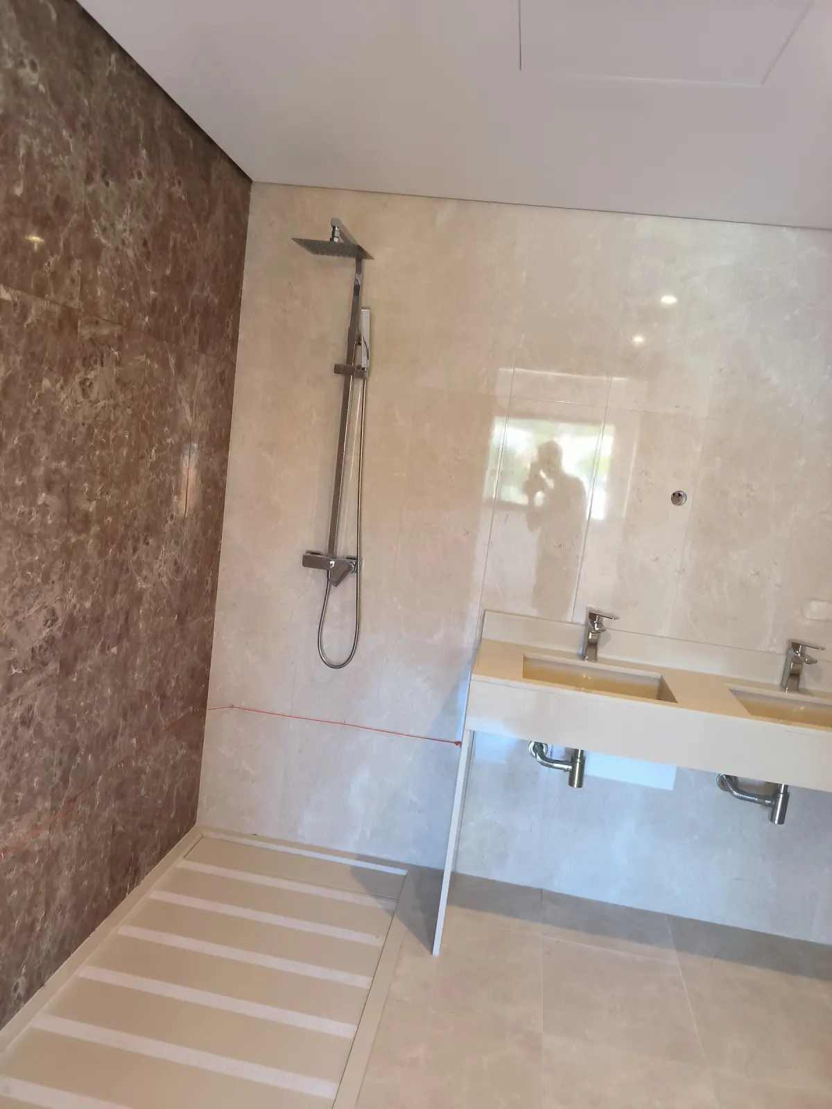 Casa de banho em mármore creme com parede de mármore castanho e duche de nível